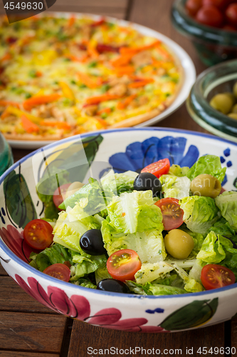Image of Small lettuce salad with pizza in background