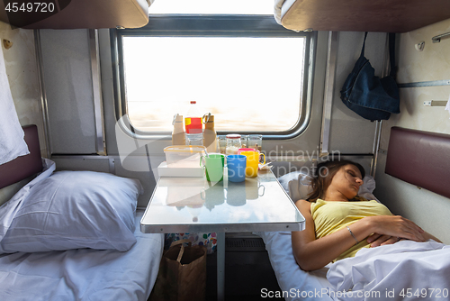 Image of Interior of a reserved seat train car, a girl sleeps on the lower shelf