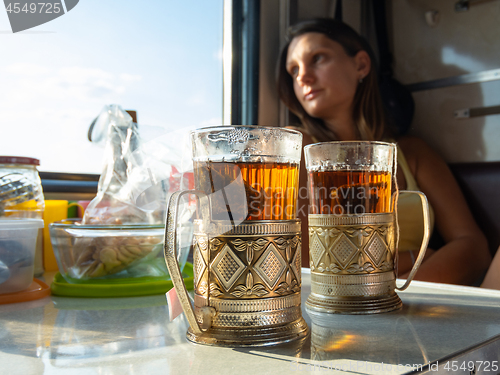 Image of On the table in the compartment of the train are glasses with tea in metal cup holders, in the background the girl looks out the window