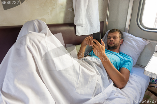 Image of A man lies on the bottom shelf in a train car with a phone in his hands