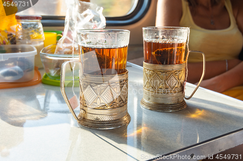 Image of On the table in the train compartment are glasses with tea in metal cup holders.