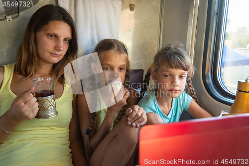 Image of Mom and two girls are looking at the laptop screen in the train car, having a bite while