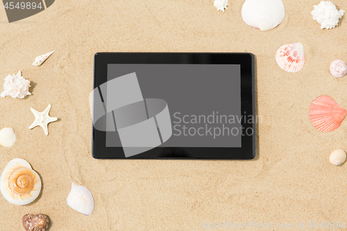 Image of tablet computer and seashells on beach sand