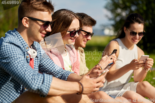 Image of smiling friends with smartphones sitting on grass