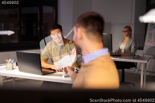 Image of man giving papers to colleague at night office