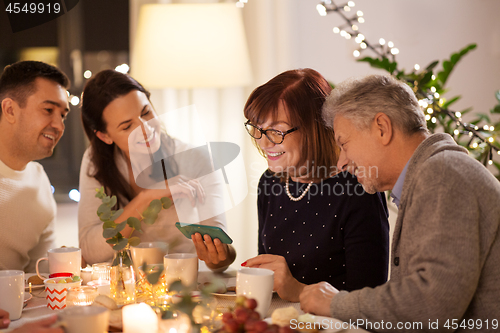 Image of happy family with smartphone at tea party at home