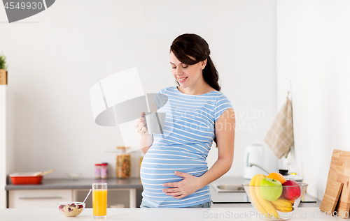 Image of happy pregnant woman with cup at home kitchen