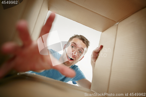 Image of Man smiling, unpacking and opening carton box and looking inside