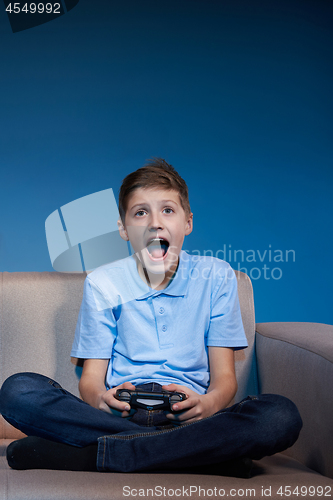 Image of Computer game competition. Gaming concept. Excited boy sitting on sofa playing video game