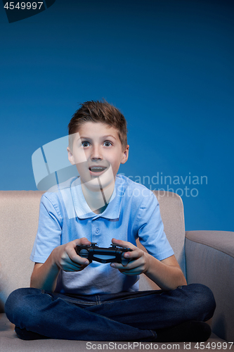 Image of Computer game competition. Gaming concept. Boy sitting on sofa playing video game with joystick