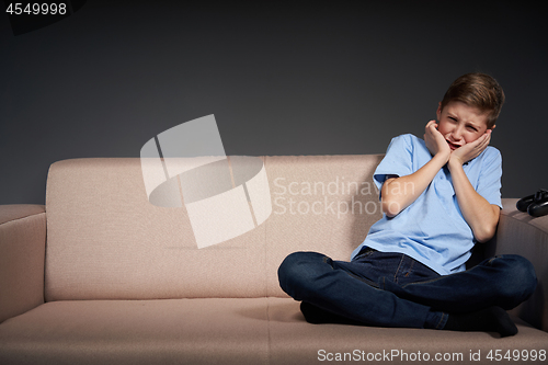 Image of Tired boy sitting on the sofa holding head in hands