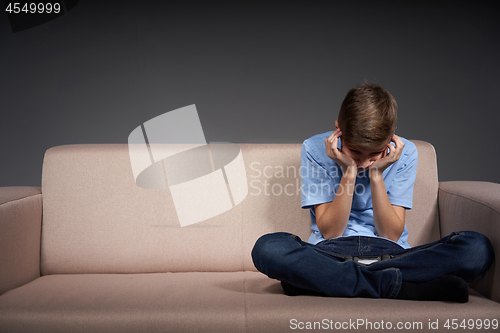 Image of Tired boy sitting on the sofa holding head in hands