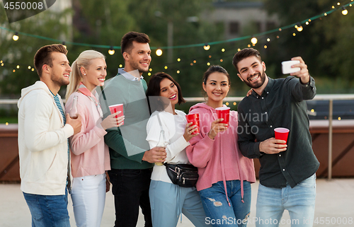 Image of friends with drinks taking selfie at rooftop party