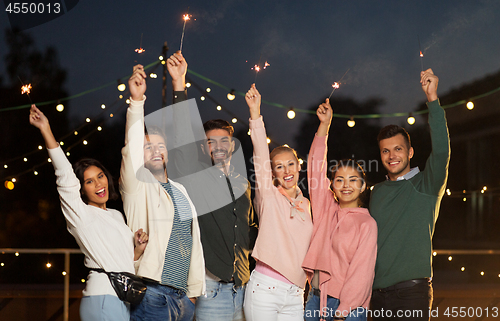 Image of happy friends with sparklers at rooftop party