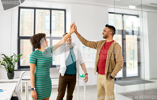 Image of happy creative team making high five at office