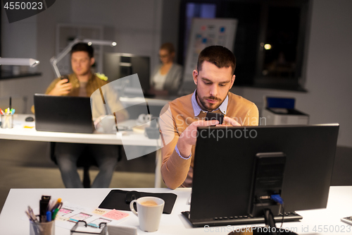 Image of man with smartphone working late at night office