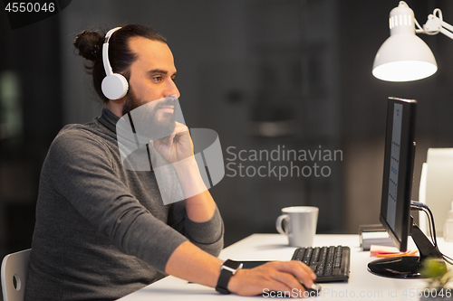 Image of creative man in headphones working at night office