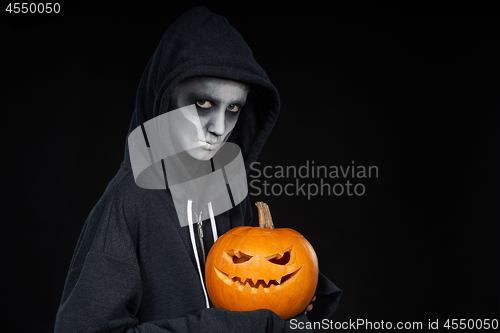 Image of Boy with Halloween makeup holding Jack O\'Lantern pumpkin on black background