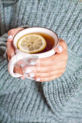 Image of Female hands holding mug of hot tea with lemon in morning.