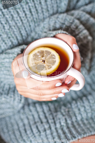 Image of Female hands holding mug of hot tea with lemon in morning.
