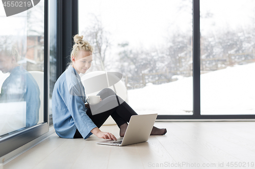 Image of woman drinking coffee and using laptop at home