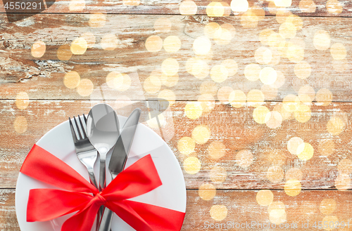 Image of cutlery tied with red ribbon on set of plates