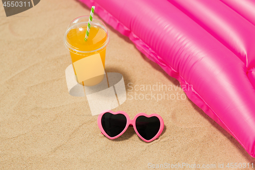 Image of sunglasses, juice and pool mattress on beach sand