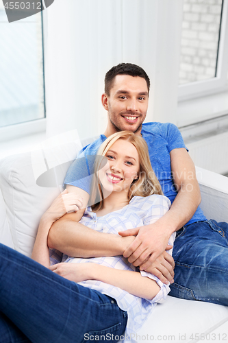 Image of happy couple sitting on sofa and hugging at home