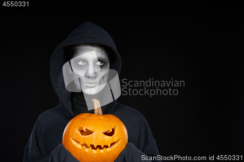 Image of Boy with Halloween makeup holding Jack O\'Lantern pumpkin on black background