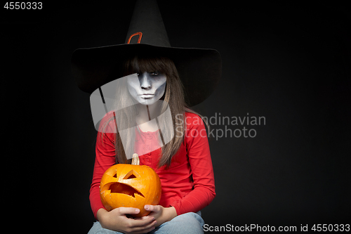 Image of Serious Halloween witch holding Jack O\'Lantern pumpkin looking at camera