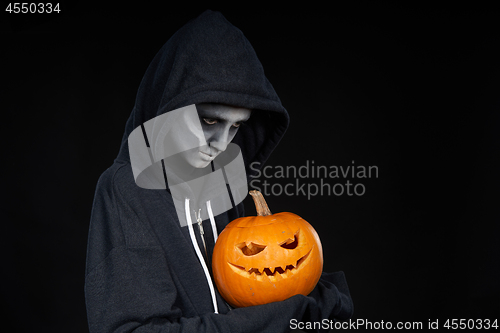 Image of Boy with Halloween makeup holding Jack O\'Lantern pumpkin on black background