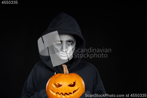 Image of Boy with Halloween makeup holding Jack O\'Lantern pumpkin on black background