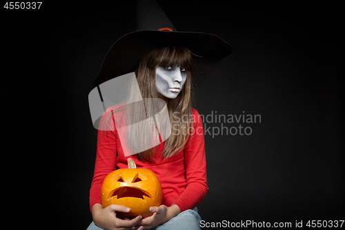 Image of Serious Halloween witch holding Jack O\'Lantern pumpkin looking at camera