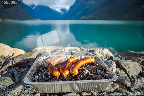 Image of Grilling sausages on disposable barbecue grid.