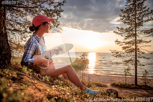 Image of Woman at sunset playing the ukulele