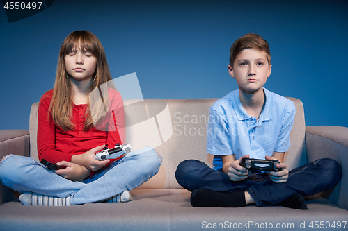 Image of Children sitting on sofa playing video game with joysticks