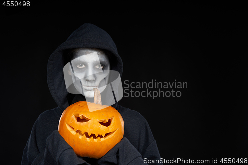 Image of Boy with Halloween makeup holding Jack O\'Lantern pumpkin on black background