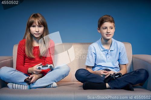 Image of Children sitting on sofa playing video game with joysticks