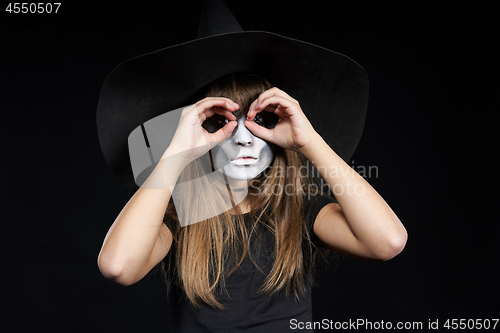 Image of Closeup of Halloween witch girl looking at camera through fingers making binoculars