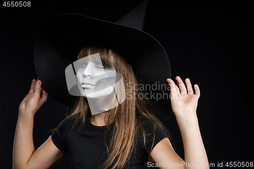 Image of Closeup of Halloween witch girl looking at camera on black background.