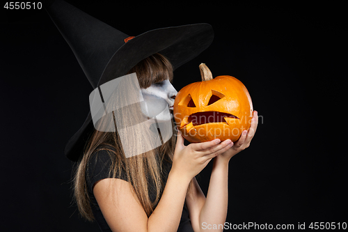 Image of Halloween witch girl giving a kiss to Jack-O-Lantern pumpkin