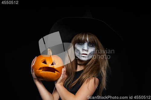 Image of Serious Halloween witch holding Jack-O-Lantern pumpkin looking at camera