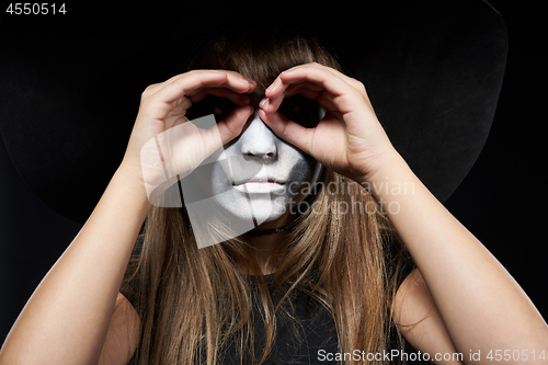 Image of Closeup of Halloween witch girl looking at camera through fingers making binoculars