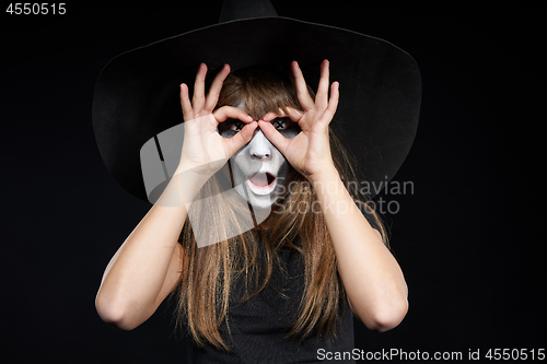 Image of Closeup of Halloween witch girl looking at camera through fingers making binoculars
