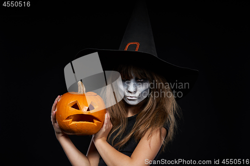 Image of Serious Halloween witch holding Jack-O-Lantern pumpkin looking at camera