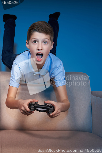 Image of Excited boy lying on sofa back playing video game with joystick