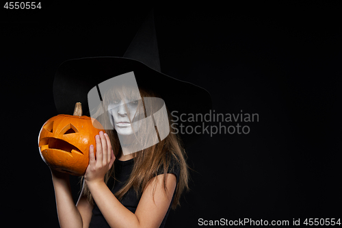 Image of Serious Halloween witch holding Jack-O-Lantern pumpkin looking at camera