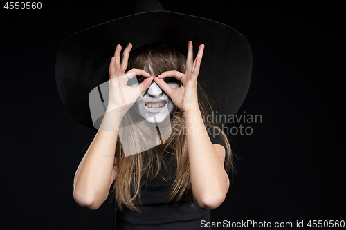 Image of Closeup of Halloween witch girl looking at camera through fingers making binoculars