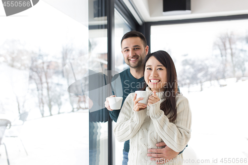 Image of multiethnic couple enjoying morning coffee by the window