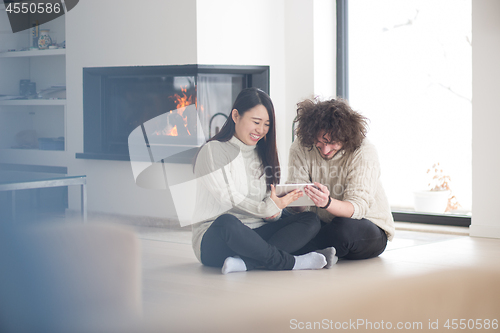 Image of multiethnic couple using tablet computer in front of fireplace